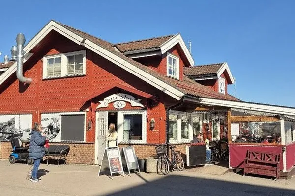 Det røde trehuset til Susa’s Kro på brygga, med skiltet over døra og den innglassede verandaen