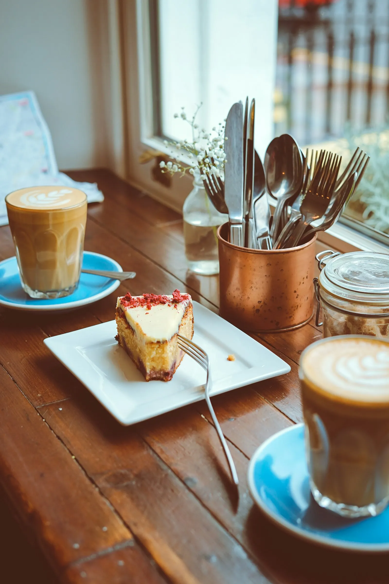 Et kakestykke og to kaffe latte på et trebord ved vinduet